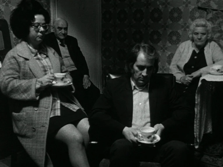 Children (1976) movie still: medium — A dimly lit room features patterned wallpaper and four adults sitting with tea. The group members sit in…