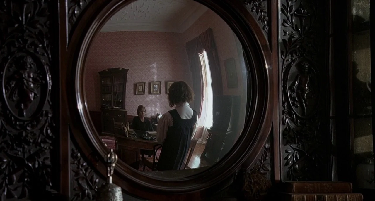 Cracks (2009) movie still: medium — A study with floral patterned wallpaper and ornate dark wood furniture features a round mirror. A young girl…