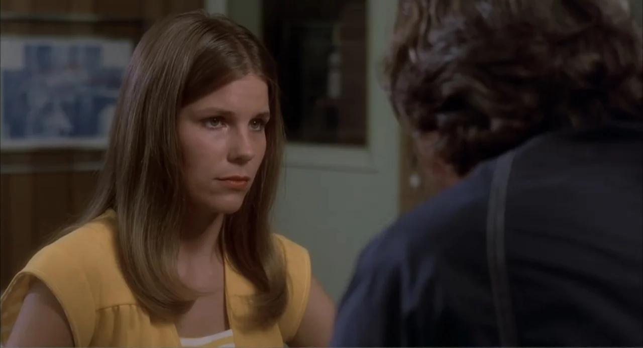Empire of the Ants (1977) movie still: medium — A domestic interior with wood-paneled walls and a framed picture hanging in the background. A woman…