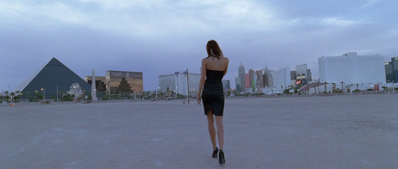 Knight of Cups (2015) movie still: fullbody — A vast, empty, dusty lot sits in front of the Las Vegas strip at twilight. A woman in a black dress…