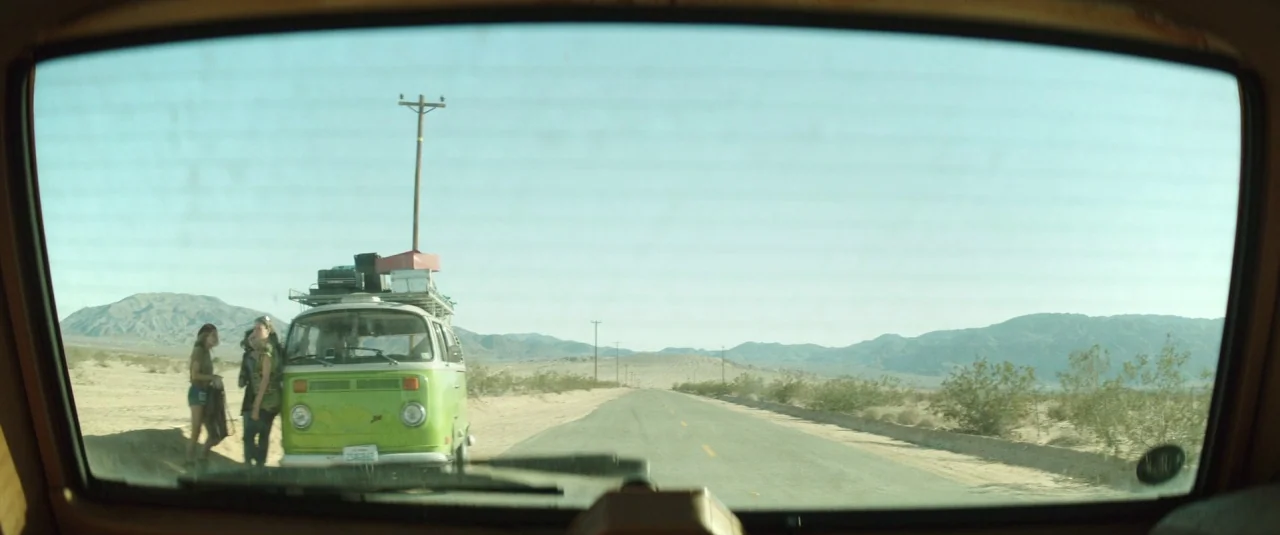 Southbound (2015) movie still: wide — A green vintage van is parked on the shoulder of a desolate desert road. Two young women stand next to the…