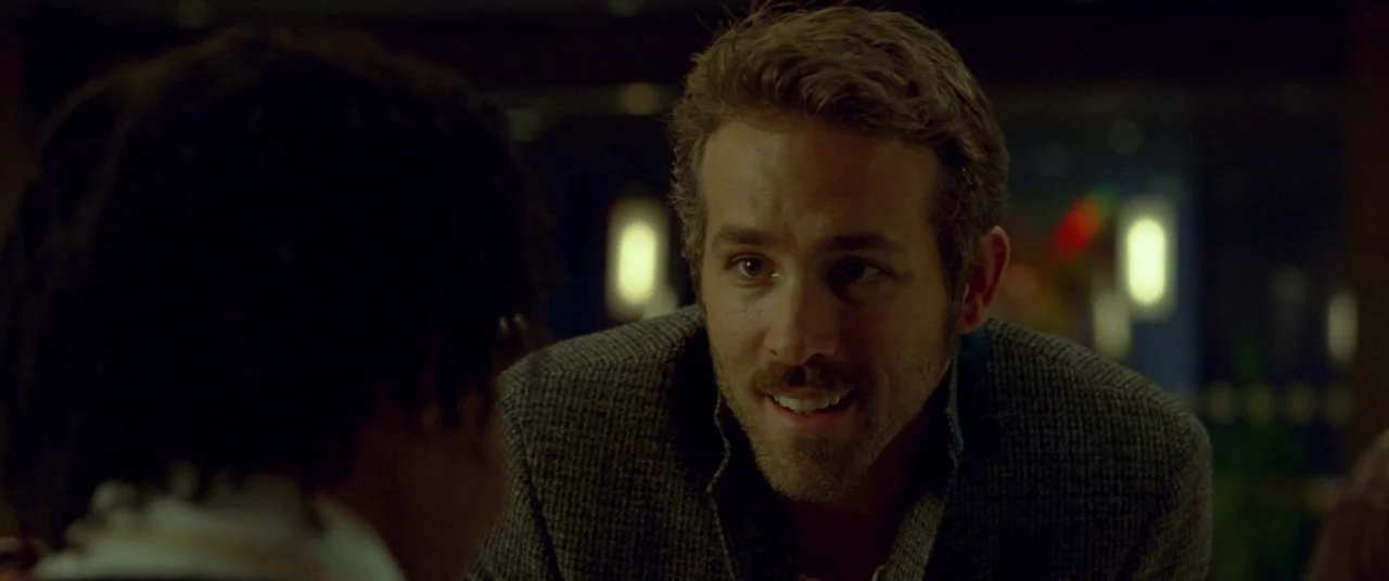 Mississippi Grind (2015) movie still: medium — An interior space with dim, blurred lighting indicating a public venue. A man with a mustache wearing…