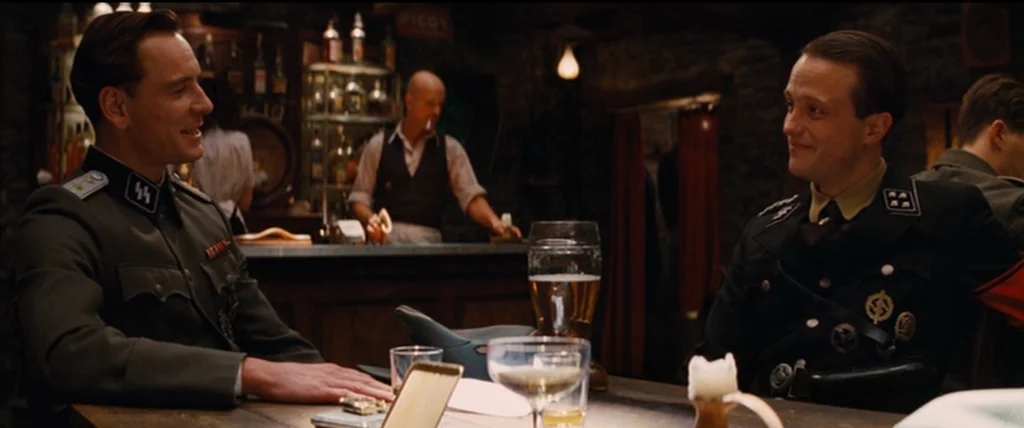 Inglourious Basterds (2009) movie still: medium — A dimly lit tavern with a stone wall and wooden bar in the background. Two uniformed military men…