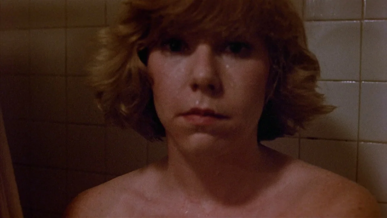 Friday the 13th Part 2 (1981) movie still: closeup — A close-up shot shows a woman in a tiled shower stall. The woman stares forward with a wet face…