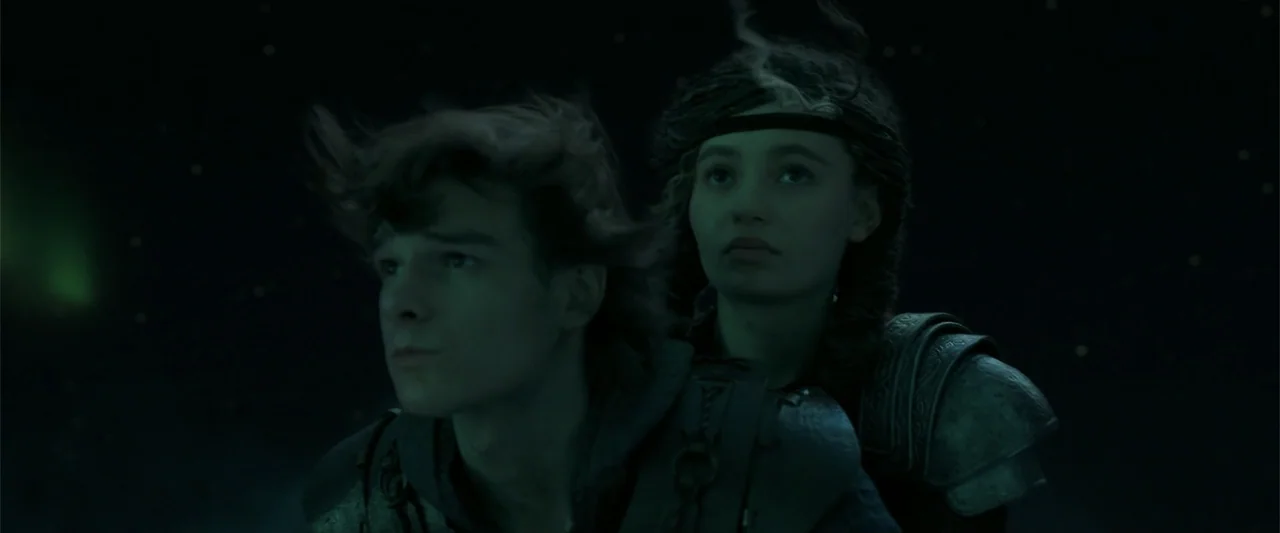 How to Train Your Dragon (2025) movie still: medium — Two individuals wearing dark leather armor travel through a vast, dark night sky. The figures…