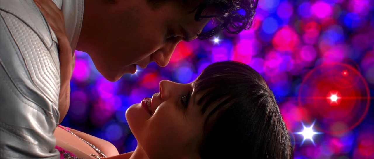 Speed Racer (2008) movie still: closeup — A dark, out-of-focus background displays bright pink and blue bokeh light circles. A man in a silver…