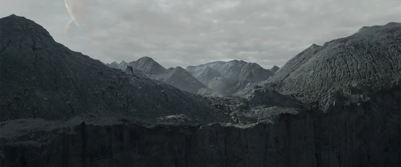 DISTANT (2026) movie still: establishing — A vast mountain range with rugged, dark rock formations under a cloudy sky. The terrain is barren and…
