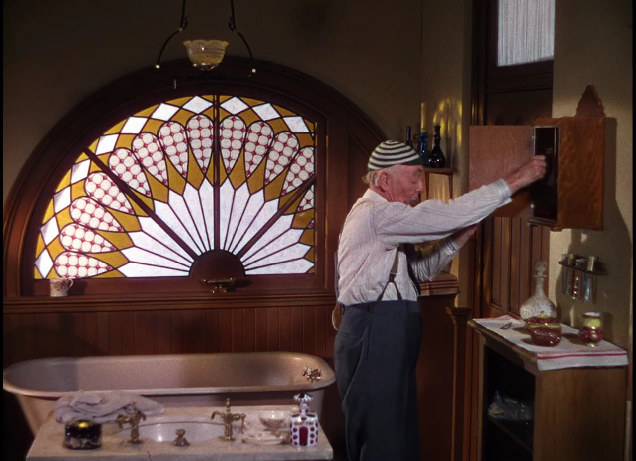 Meet Me In St. Louis (1944) movie still: medium — An interior bathroom featuring a large semi-circular stained glass window and wood paneling. An…