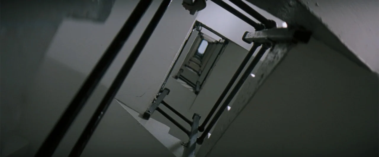 The Pelican Brief (1993) movie still: establishing — A vertical view looking up through the rectangular center of a stairwell structure. Stark white…