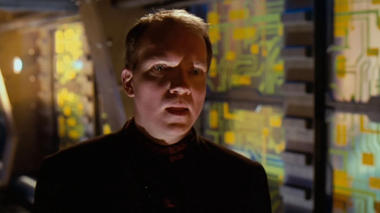 Jason X (2001) movie still: medium — An interior space features walls lined with glowing yellow electronic circuit board displays. A man in dark…