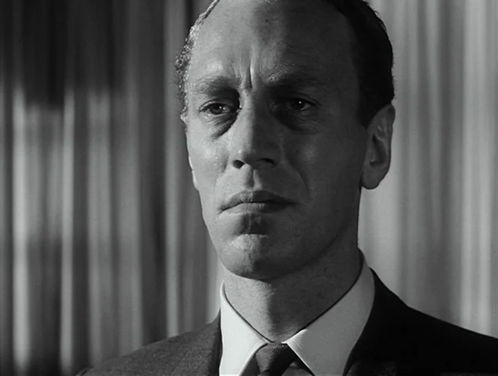 Hour of the Wolf (1968) movie still: closeup — An indoor office space features pleated vertical curtains visible in the blurred background. A…