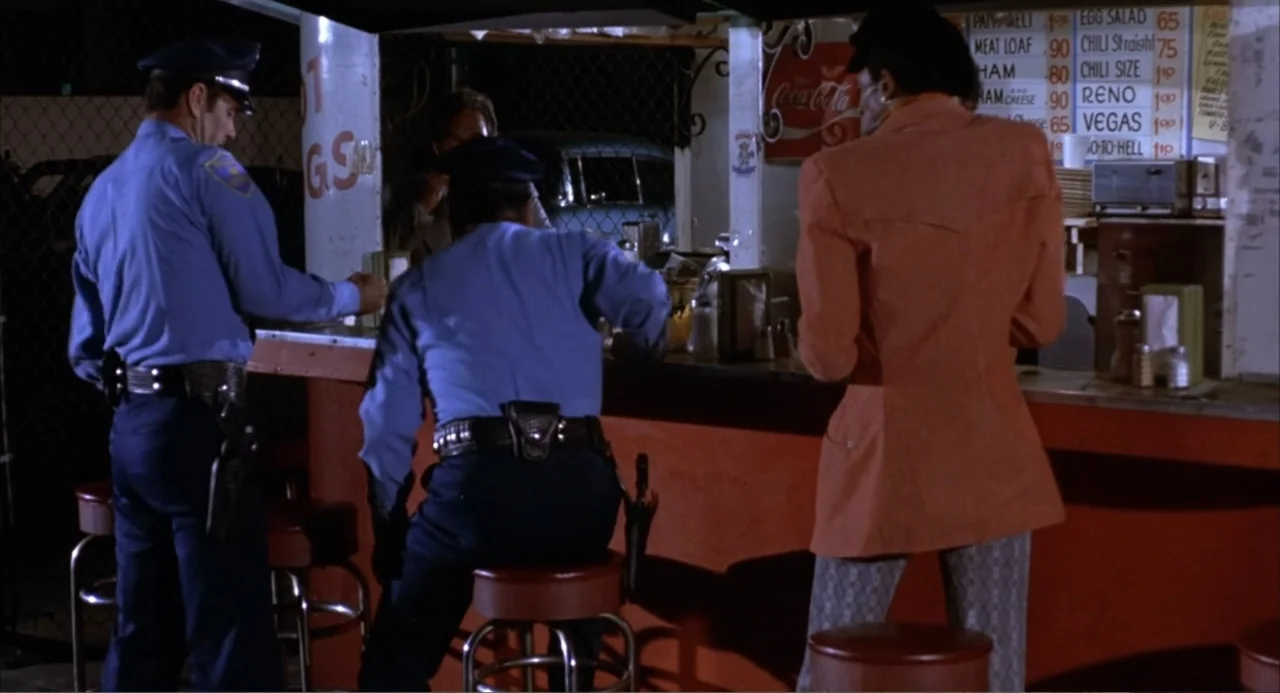 Foxy Brown (1974) movie still: medium — A late-night roadside diner features a red counter and a menu posted on the wall. Two uniformed police…