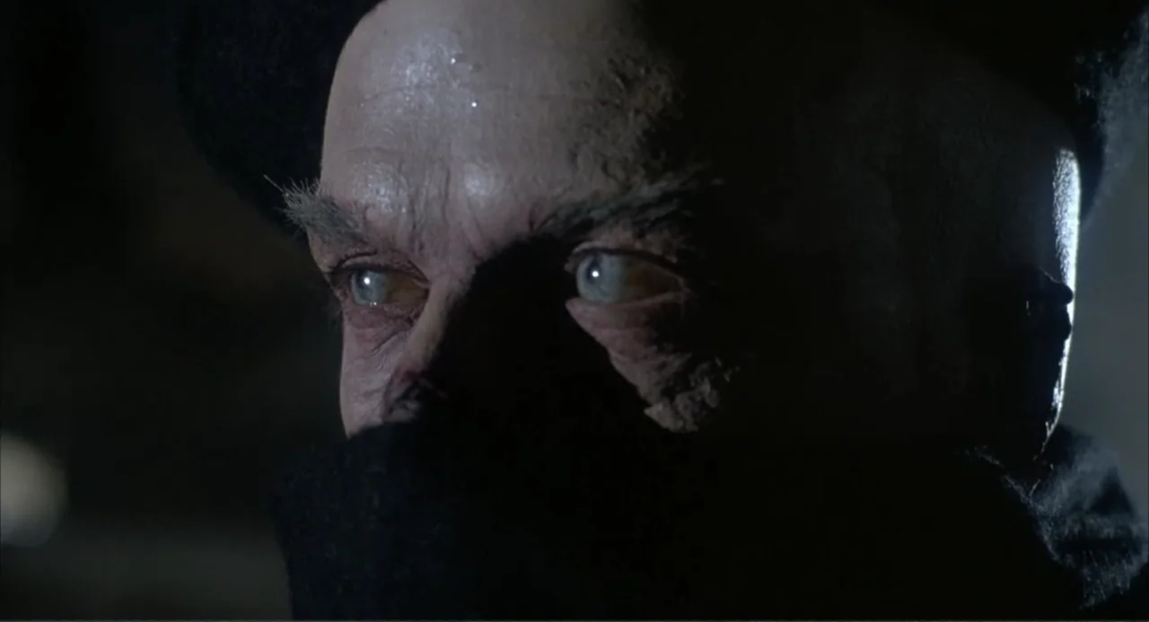I, Madman (1989) movie still: closeup — A dimly lit environment with dark, indistinct surroundings framing a close portrait of a man. The subject…