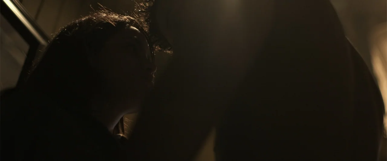 Kimura (2017) movie still: closeup — Two individuals stand in a dimly lit interior space with soft light hitting them. They face one another closely…