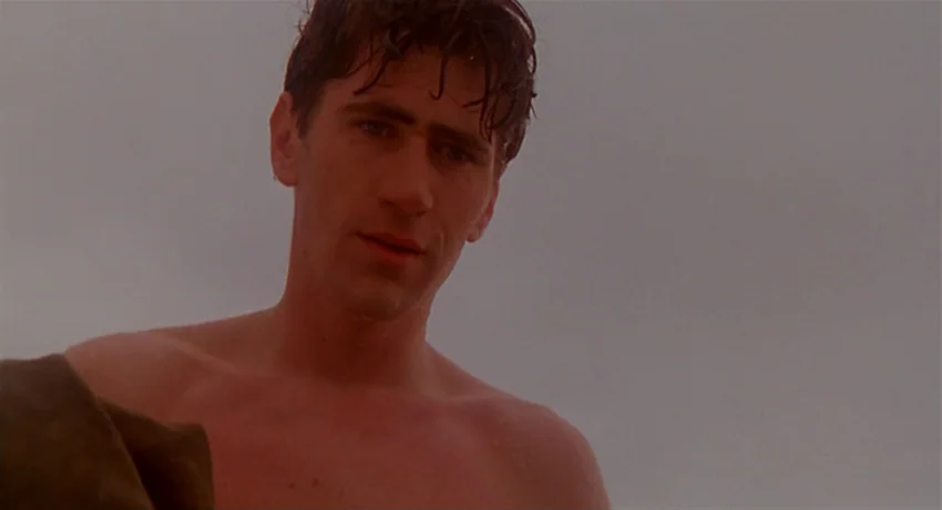 The Secret Of Roan Inish (1994) movie still: medium — An open beach setting features a cloudy, washed-out sky as a backdrop. A young, wet-haired man…