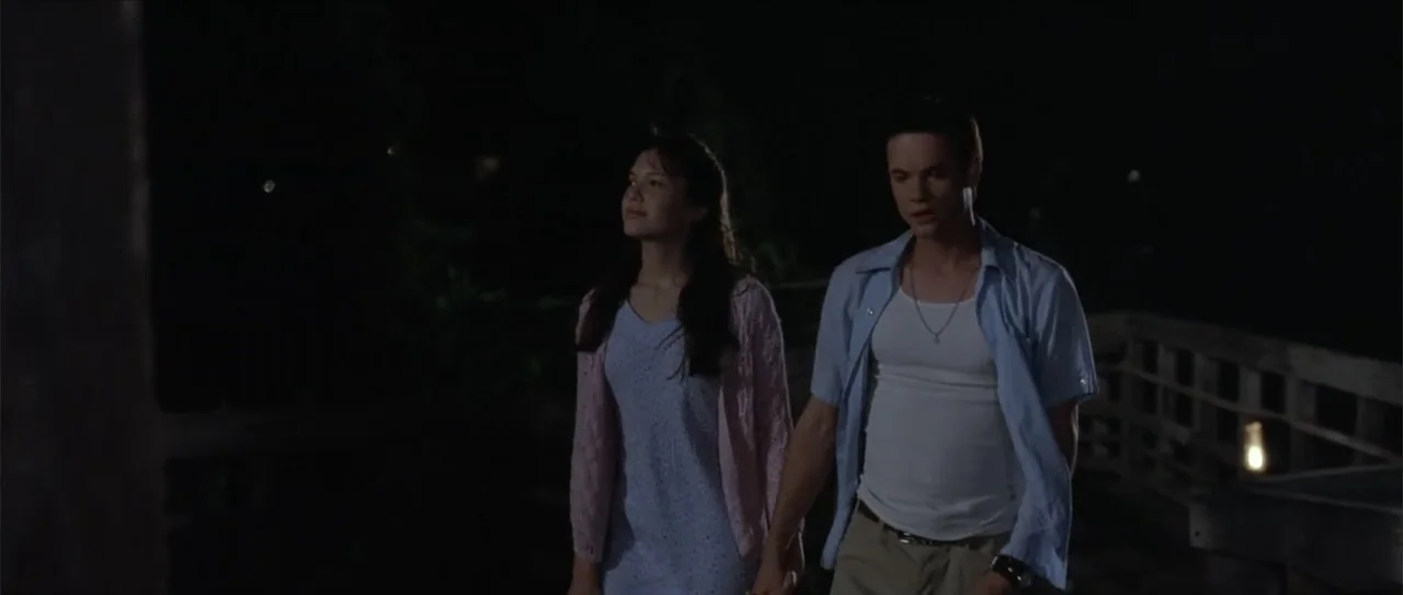 A Walk to Remember (2002) movie still: medium — A dark outdoor pier at night with wooden railings and dim perimeter lights. A young man and woman…
