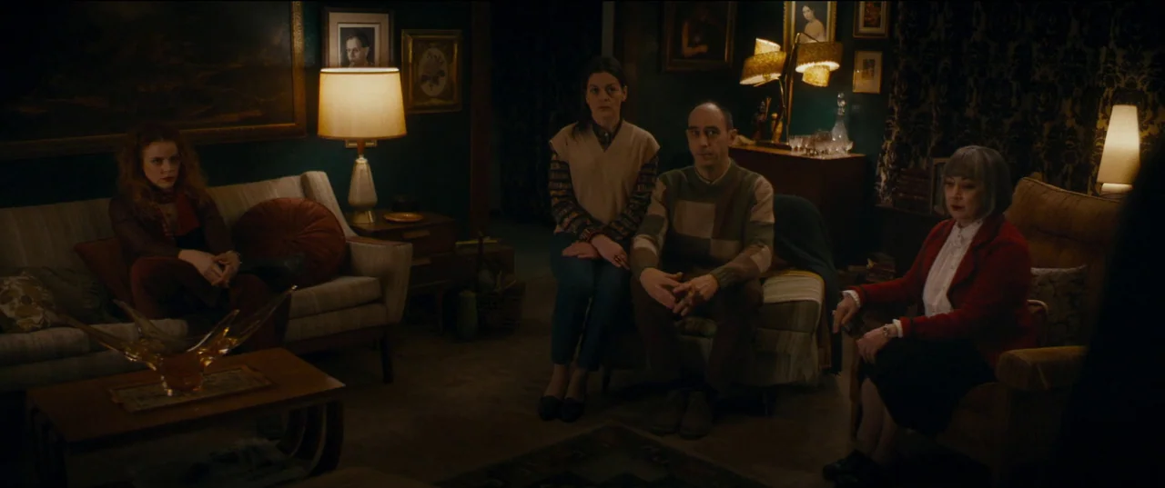 Humanist Vampire Seeking Consenting Suicidal Person (2023) movie still: wide — A dimly lit 1970s living room features dark green walls, vintage…