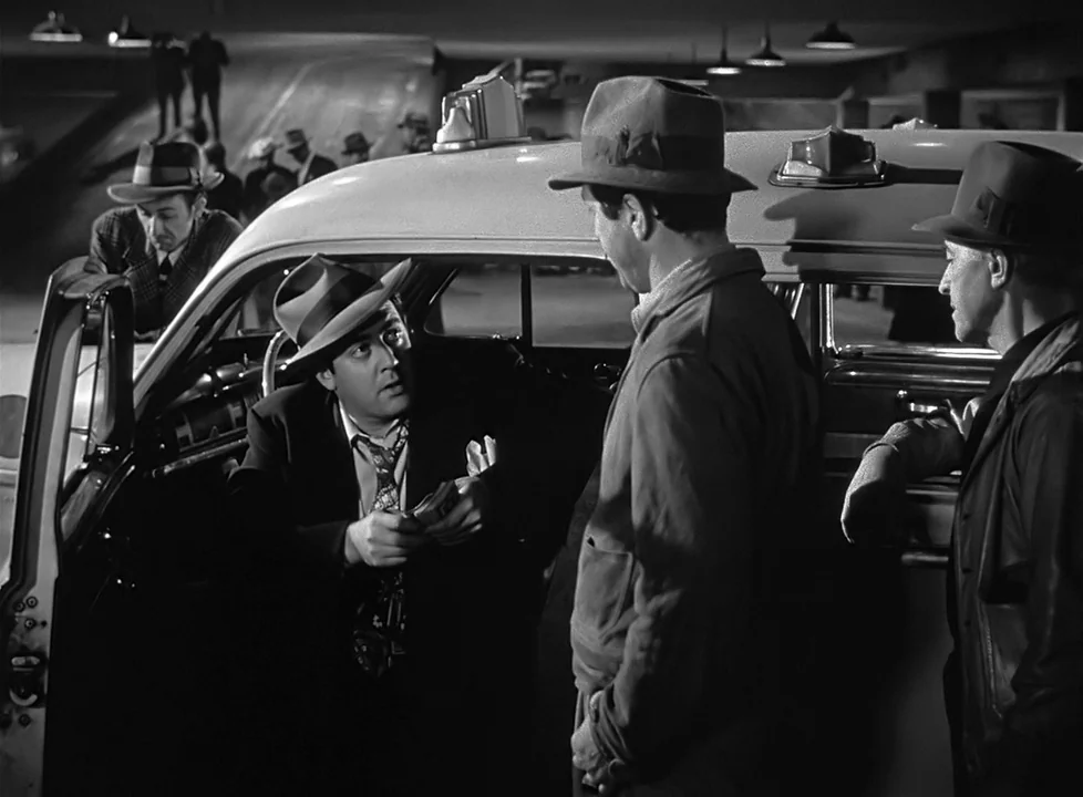M (1951) (1951) movie still: medium — A dimly lit parking garage features a vintage taxi under bright overhead lights. Three men in fedoras converse…