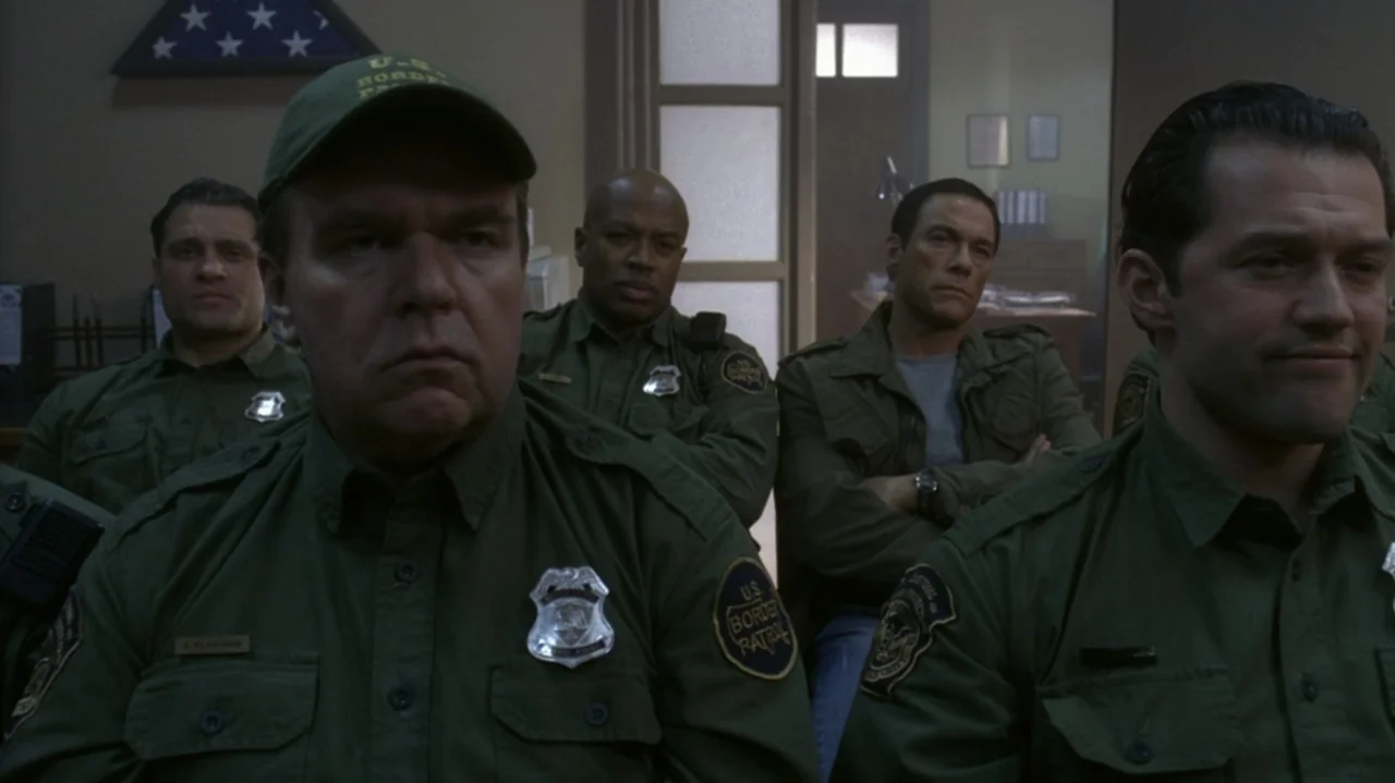 The Shepherd (2023) movie still: medium — A group of men in green uniforms sit inside a room with simple walls. They look toward the front of the…