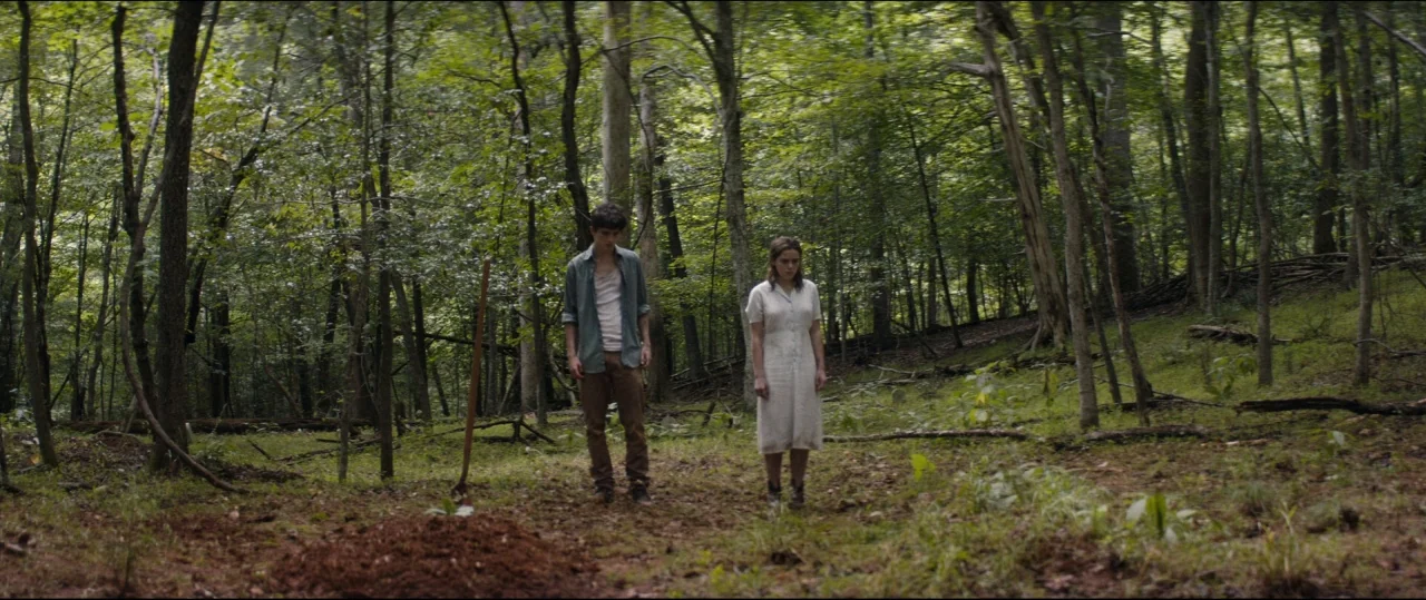 One & Two (2015) movie still: fullbody — A clearing in a dense woodland area with scattered leaves and fresh soil mounds. A young man and woman…