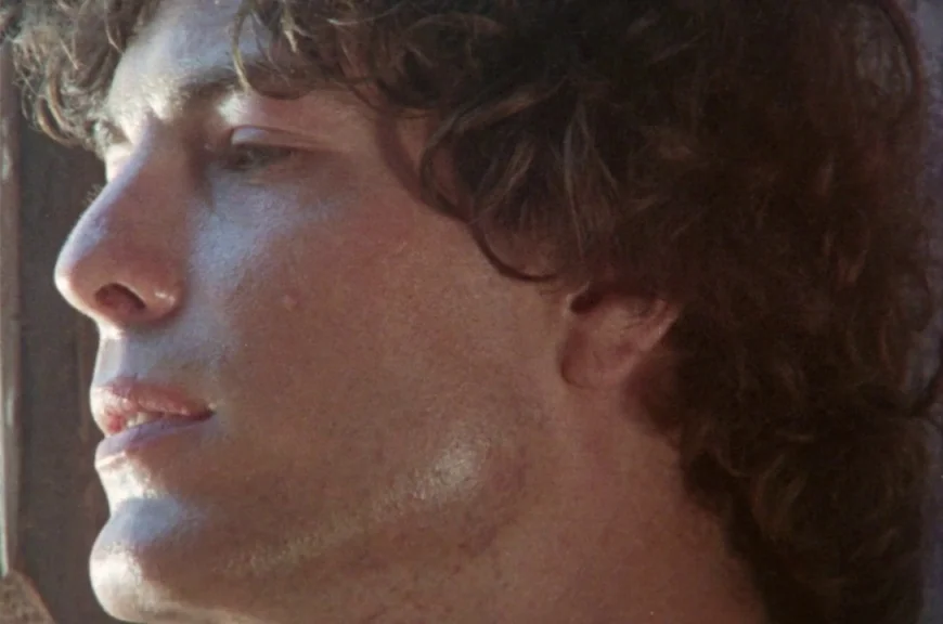 Sebastiane (1976) movie still: closeup — A close-up profile view of a young man with curly brown hair. The subject gazes away from the lens while…
