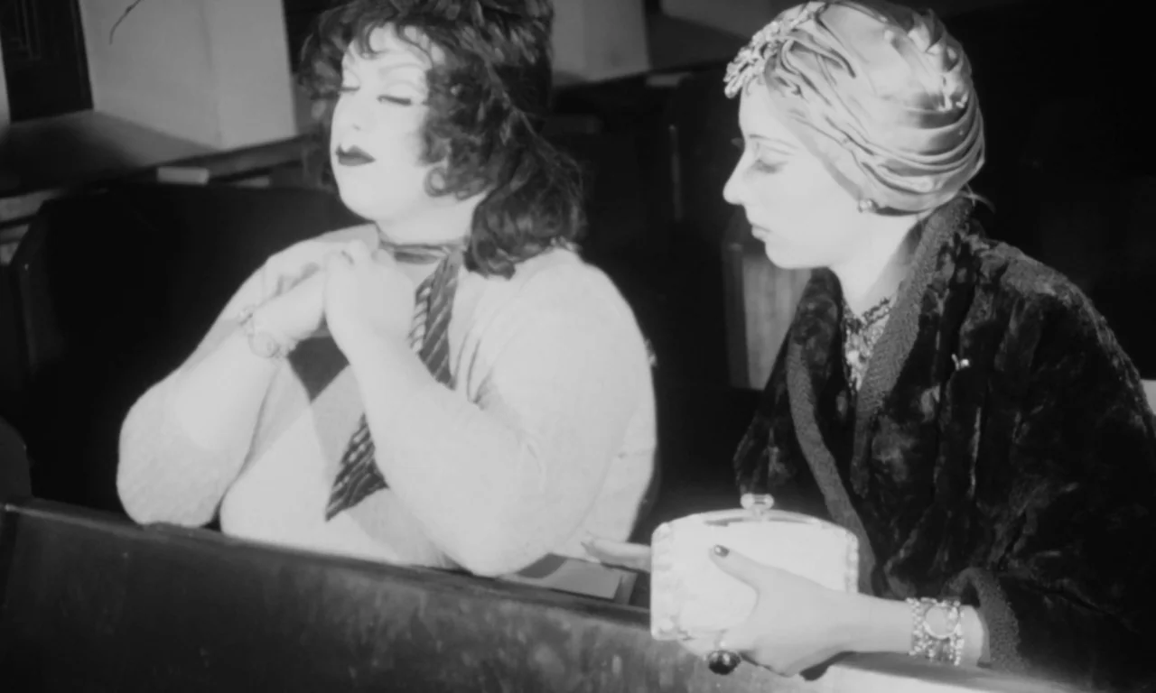 Multiple Maniacs (1970) movie still: medium — Two women sit side by side in a wooden church pew in the 1920s. They are positioned near each other…