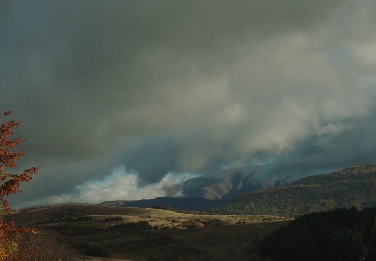 You Won’t Be Alone (2022) movie still: establishing — A rolling mountain landscape features dry, grassy slopes under a thick, dark overcast sky.…
