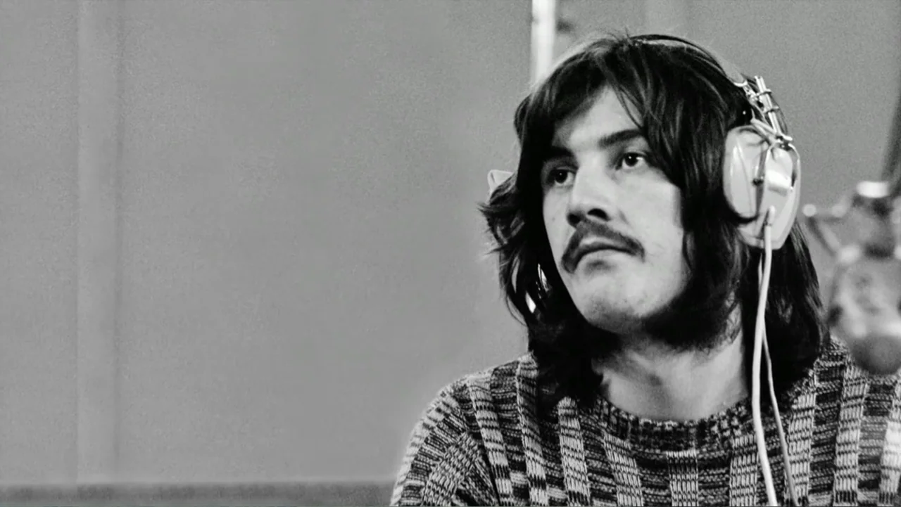Becoming Led Zeppelin (2025) movie still: closeup — A man sits in a professional recording studio wearing large over-ear vintage headphones. The man…