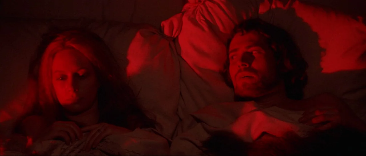 Macbeth (1971) movie still: medium — A dark bedroom with two people lying in bed under white sheets. The man looks toward the woman while the woman…