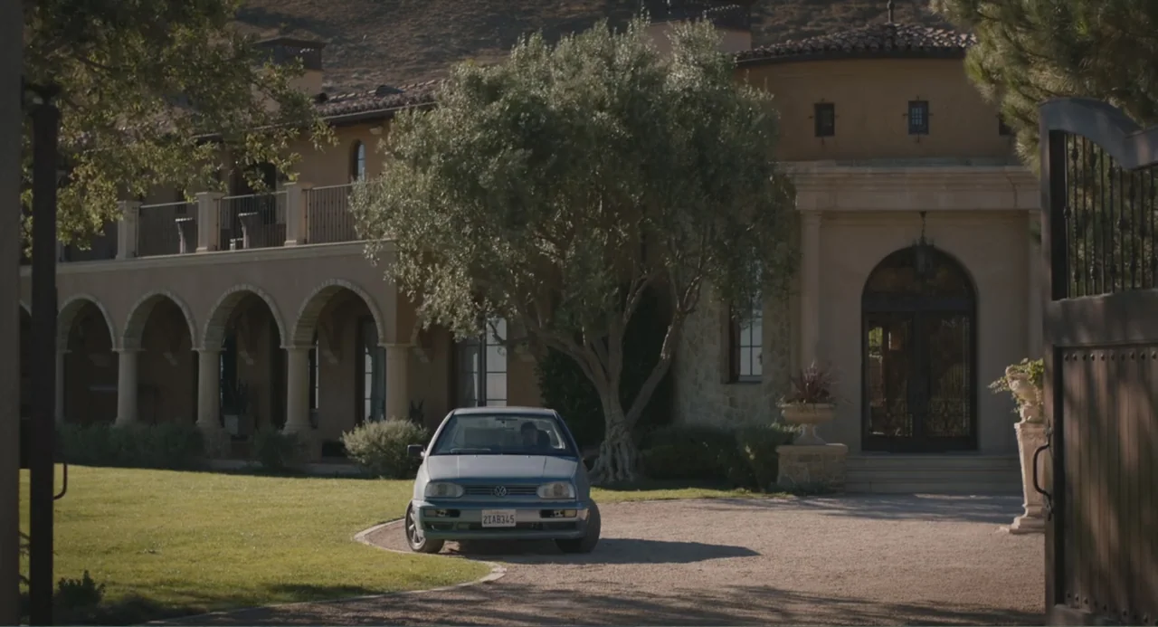Beatriz at Dinner (2017) movie still: wide — A Mediterranean-style villa with arched porches and stucco walls sits behind a gravel driveway. A light…