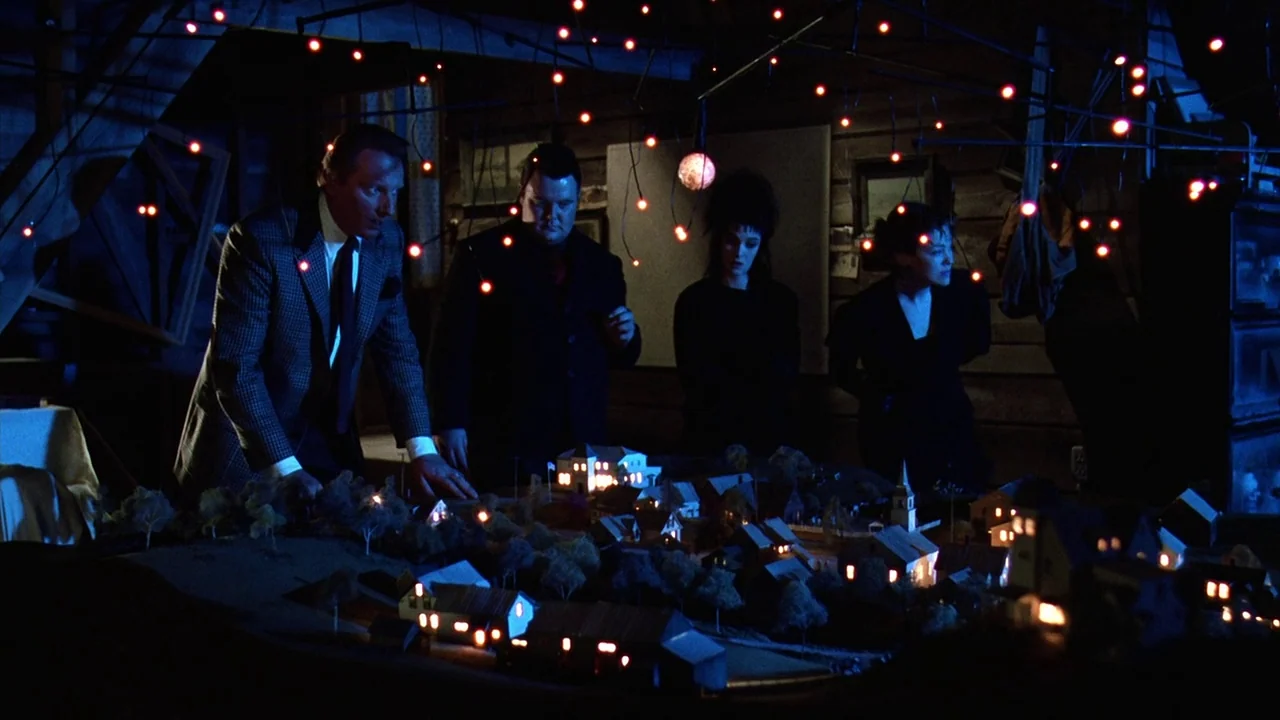 Beetlejuice (1988) movie still: wide — A dark wooden attic space is cluttered with miscellaneous items and hanging red fairy lights. Four…