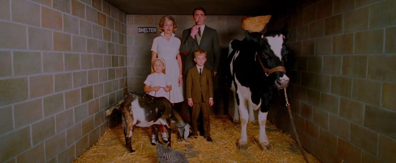 A Single Man (2009) movie still: fullbody — A rectangular room made of cinder block walls with hay covering the floor. A family of four stands in…