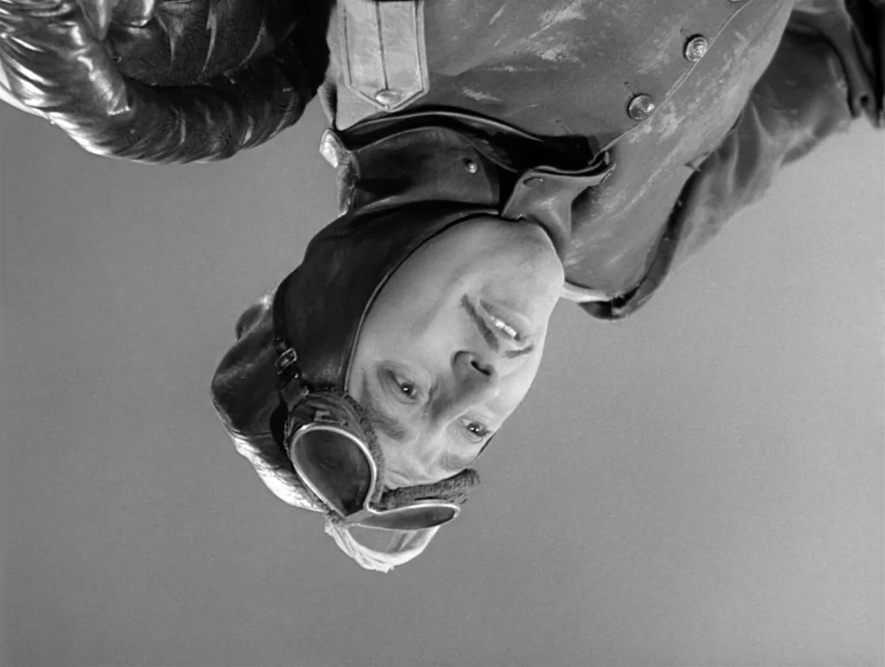 The Great Dictator (1940) movie still: closeup — An upside-down close-up shows a pilot against a featureless gray background. The man wears a…