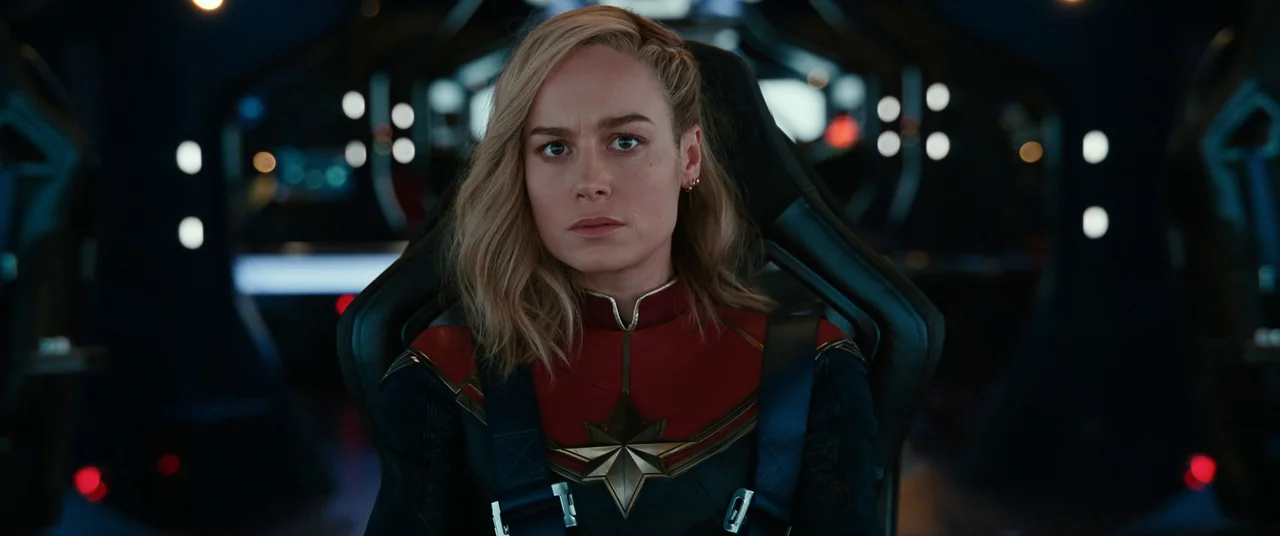 The Marvels (2023) movie still: medium — A dimly lit high-tech cockpit with dark surfaces and scattered soft circular lights. A woman in a superhero…