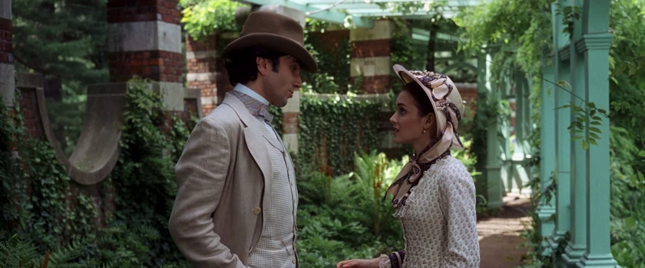 The Age of Innocence (1993) movie still: medium — A wooden lattice structure overgrown with greenery covers a gravel walkway beside brick columns. A…