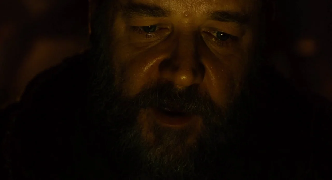 Noah (2014) movie still: closeup — A dark, dimly lit space is dominated by the flickering light of a fire. A middle-aged man with a heavy beard…