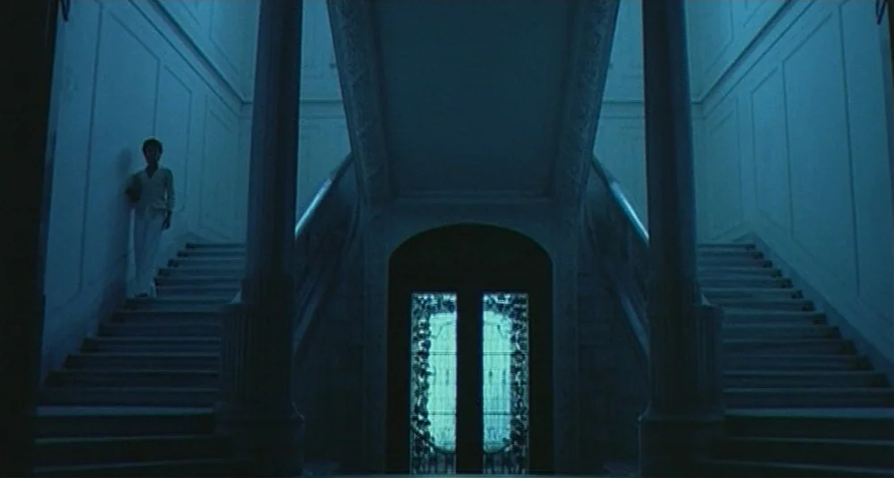 Footprints (Le Orme) (1975) movie still: wide — A grand, symmetrical interior staircase features dual flights of stairs meeting at a landing. A…