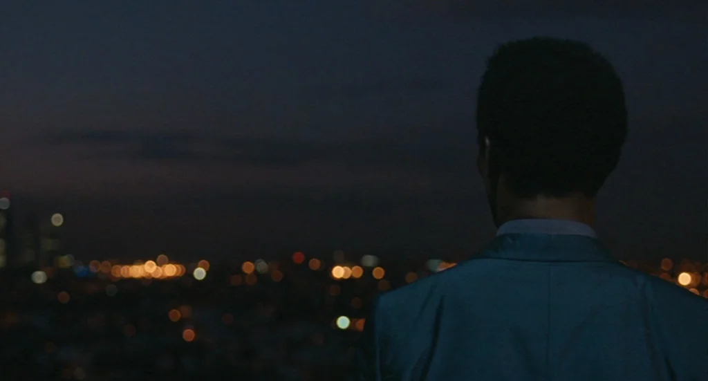 The Limits of Control (2009) movie still: medium — A man stands on a dark rooftop looking out over an urban horizon at night. The city lights appear…