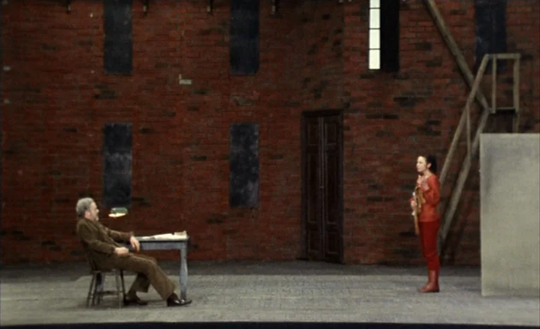 After The Rehearsal (1984) movie still: wide — A minimalist studio set features a large red brick wall with dark rectangular apertures. An older man…