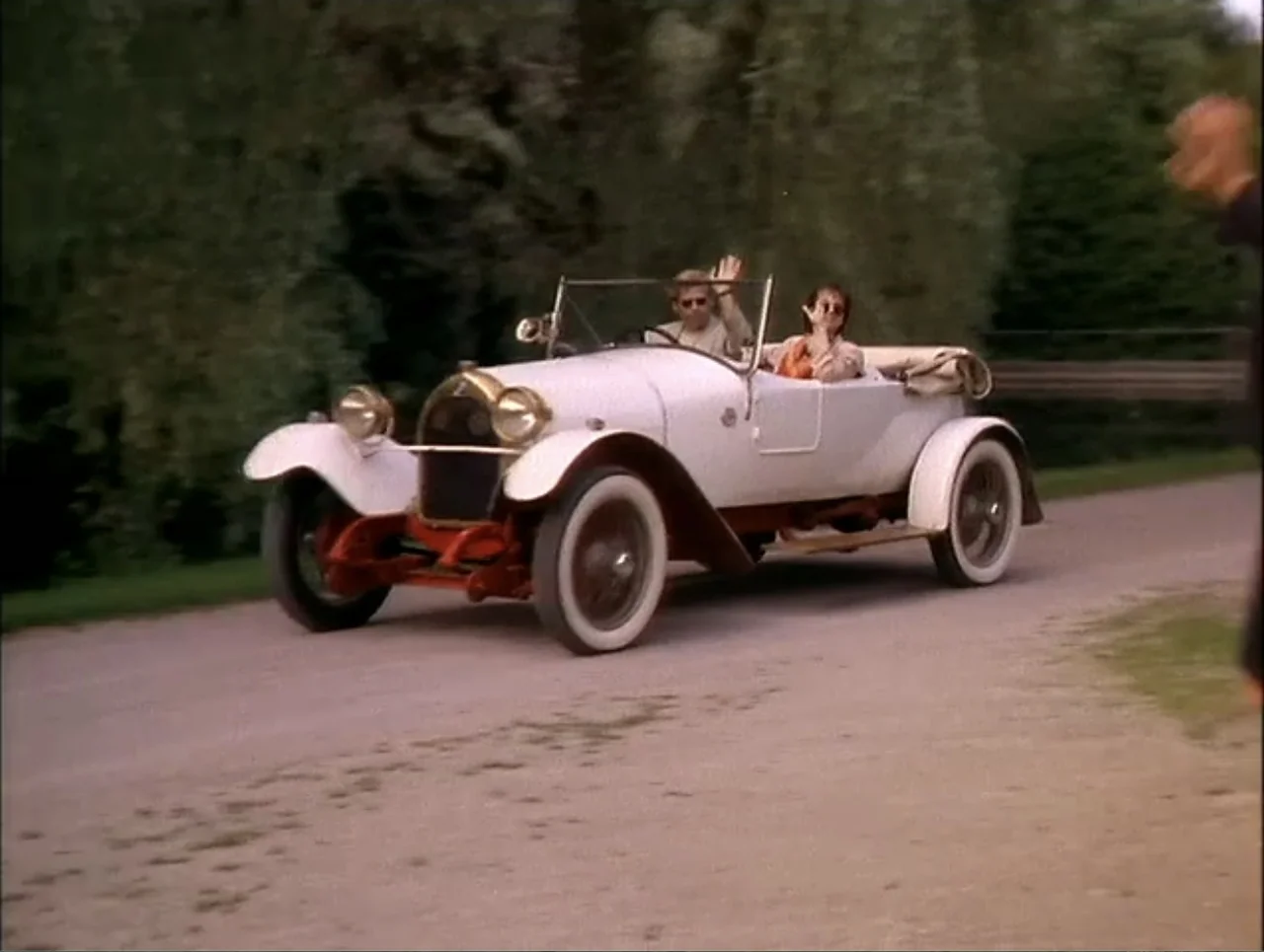 At the Midnight Hour (1995) movie still: fullbody — A cream-colored vintage convertible travels down a narrow, unpaved rural road lined with trees.…