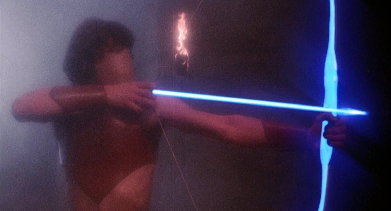 Conquest (1983) movie still: medium — A dark, smoke-filled area serves as the backdrop for a warrior with a weapon. A man in leather armor holds a…
