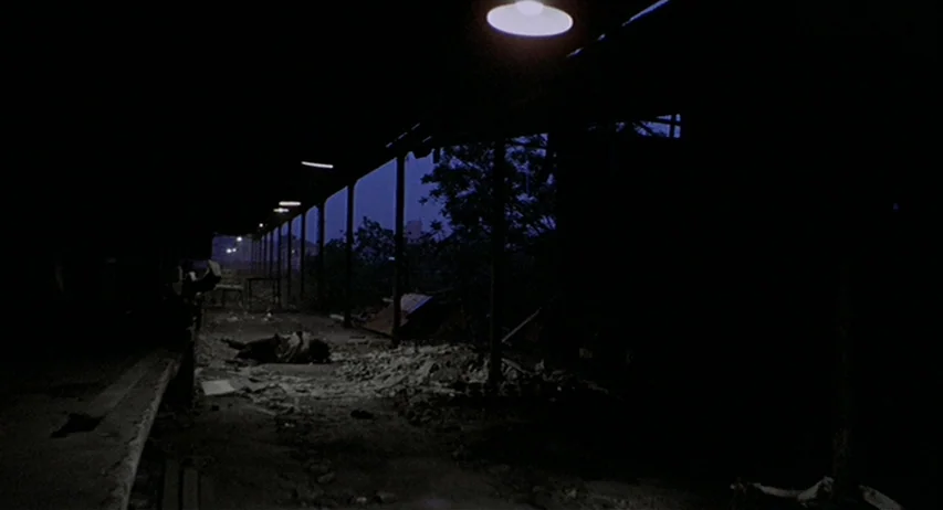 The Fifth Cord (1971) movie still: wide — An industrial loading dock at night features concrete pillars and scattered debris. A person lies on the…