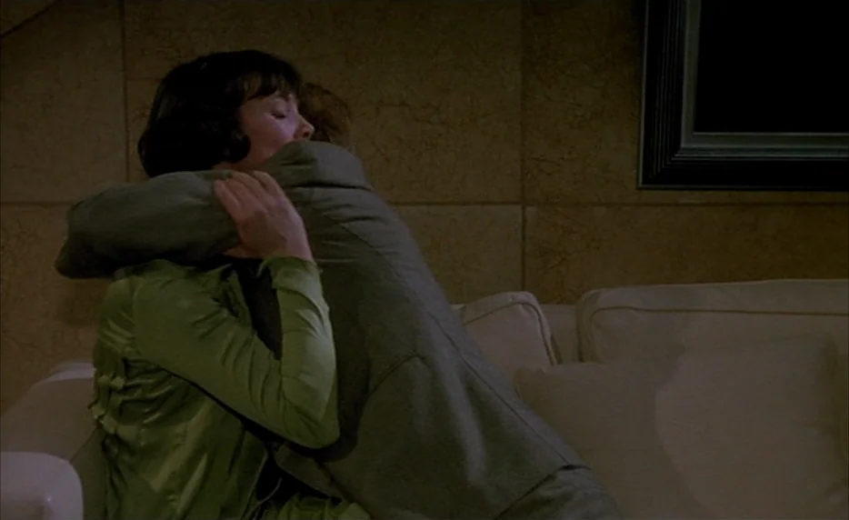 Mélo (1986) movie still: medium — An interior space with light-colored, textured walls and a cream upholstered sofa. A woman in a green top hugs a…