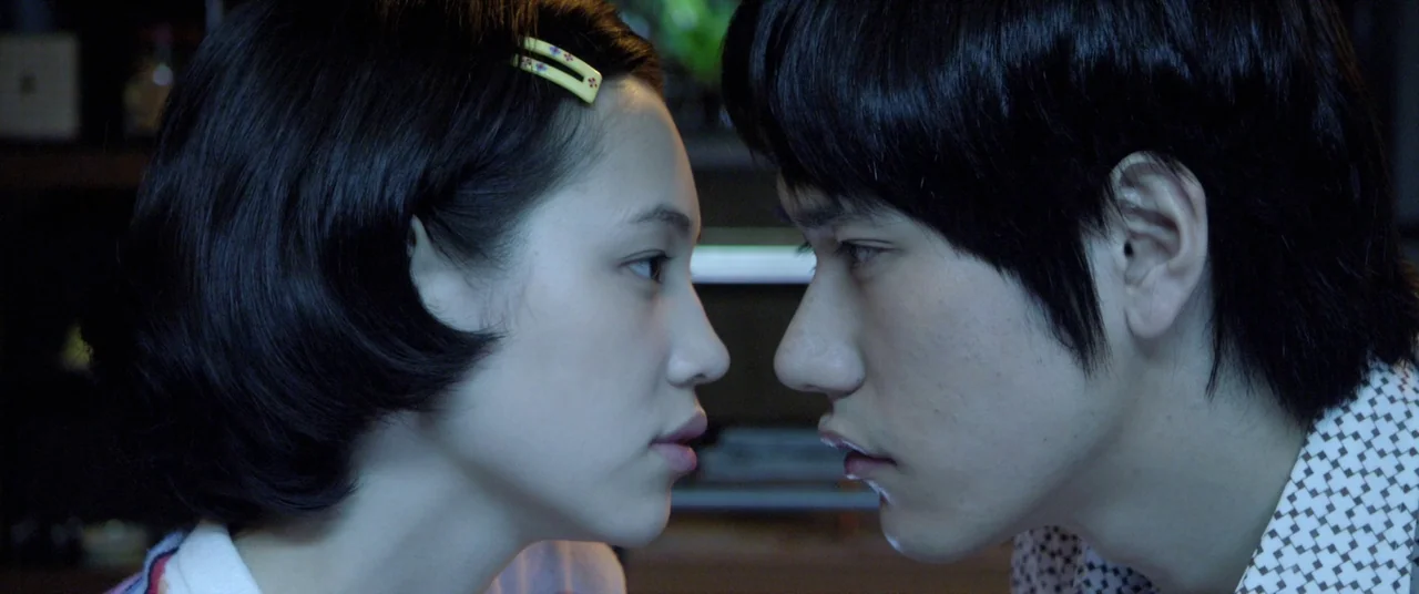 Norwegian Wood (2010) movie still: closeup — Two individuals stand facing each other in a dark indoor space. The close-up captures their profiles…