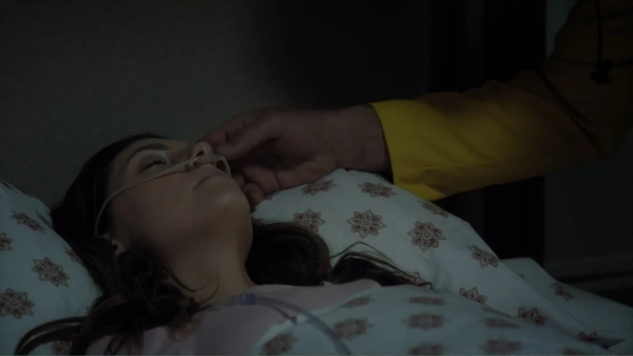 Storm Damage (2000) movie still: closeup — A woman lies in a bed with a nasal cannula in a dark room. A hand in a bright yellow sleeve reaches out…