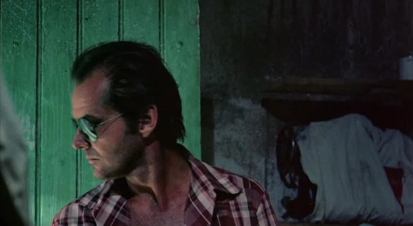 The Passenger (1975) movie still: medium — A dimly lit room features a textured concrete wall and a bright green wooden door. A man with dark…