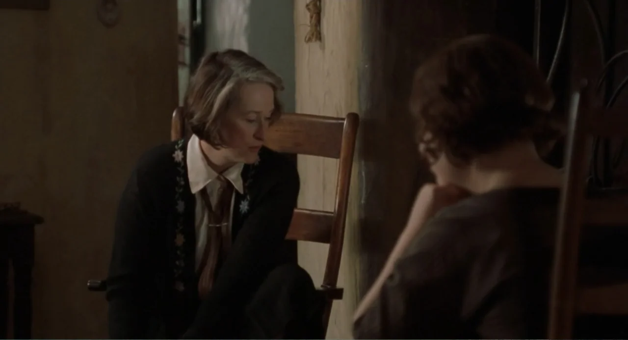 Dancing at Lughnasa (1998) movie still: medium — An interior space features wooden chairs and soft, natural light filtering through a window. Two…