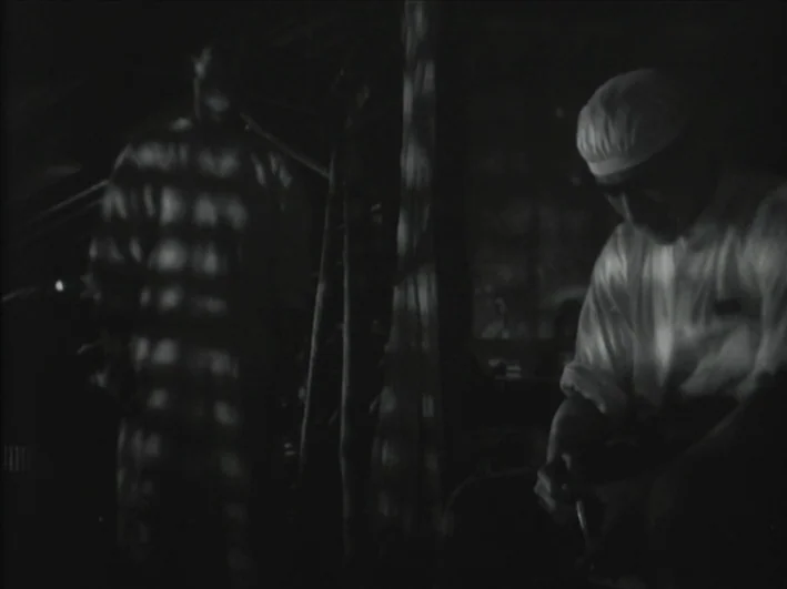 The Quiet Duel (1949) movie still: medium — A dimly lit room with barred-like shadows cast across walls and figures. One man sits in the foreground…