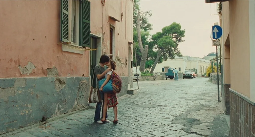 Something in the Air (2012) movie still: fullbody — A narrow Mediterranean-style cobblestone street is lined with aging, peach-colored stucco…