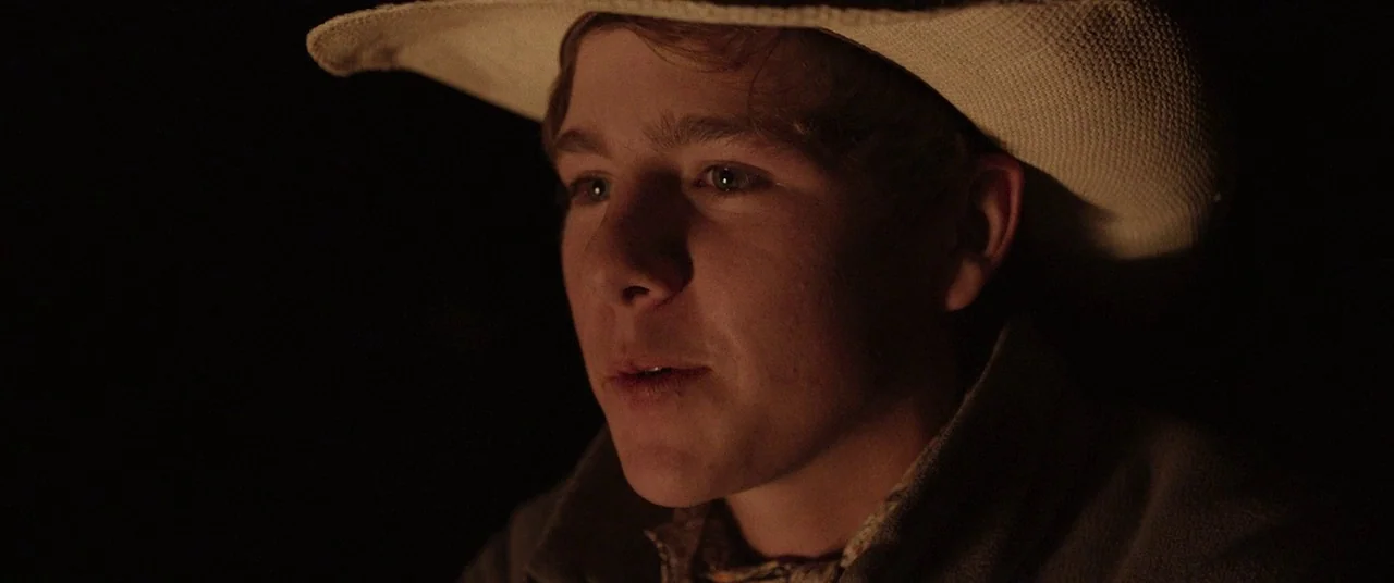 The Rider (2017) movie still: closeup — A dark environment at night with a single subject highlighted by fire. The young man wears a light-colored…